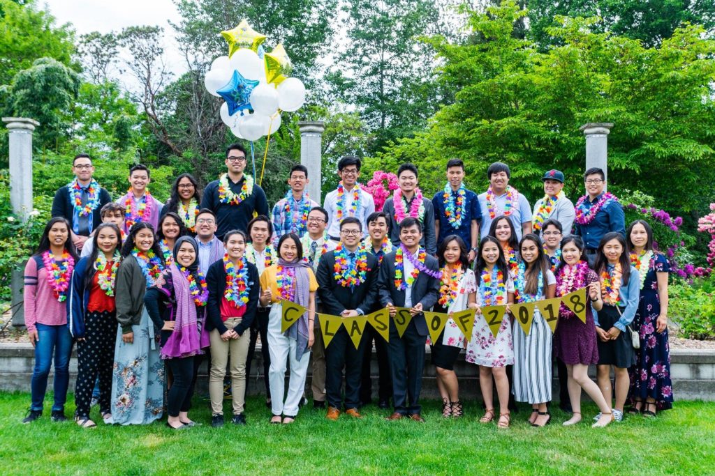 3 rows of graduates posing in front of three while pillars in Sullivan Group at the University of Washington